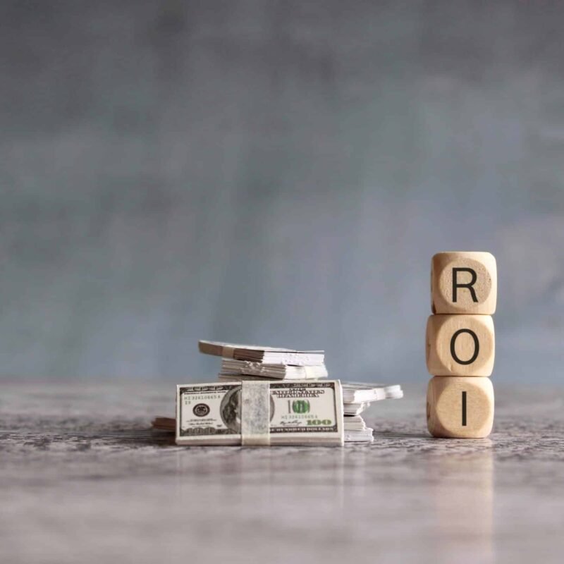 Stack of money and wooden cubes with text ROI. Return On Investment, financial and business concept